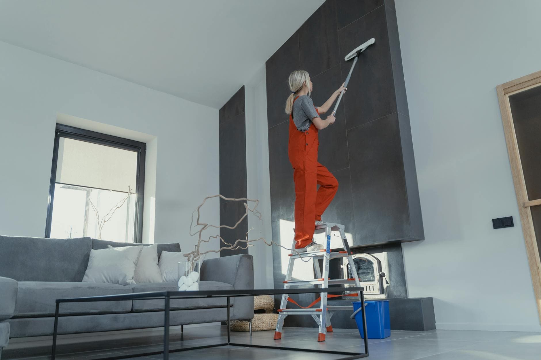 Your Business cleaner in red overalls on a ladder cleaning a high wall in a Manhattan apartment — Post-Construction Cleanup in Great Neck, Long Island