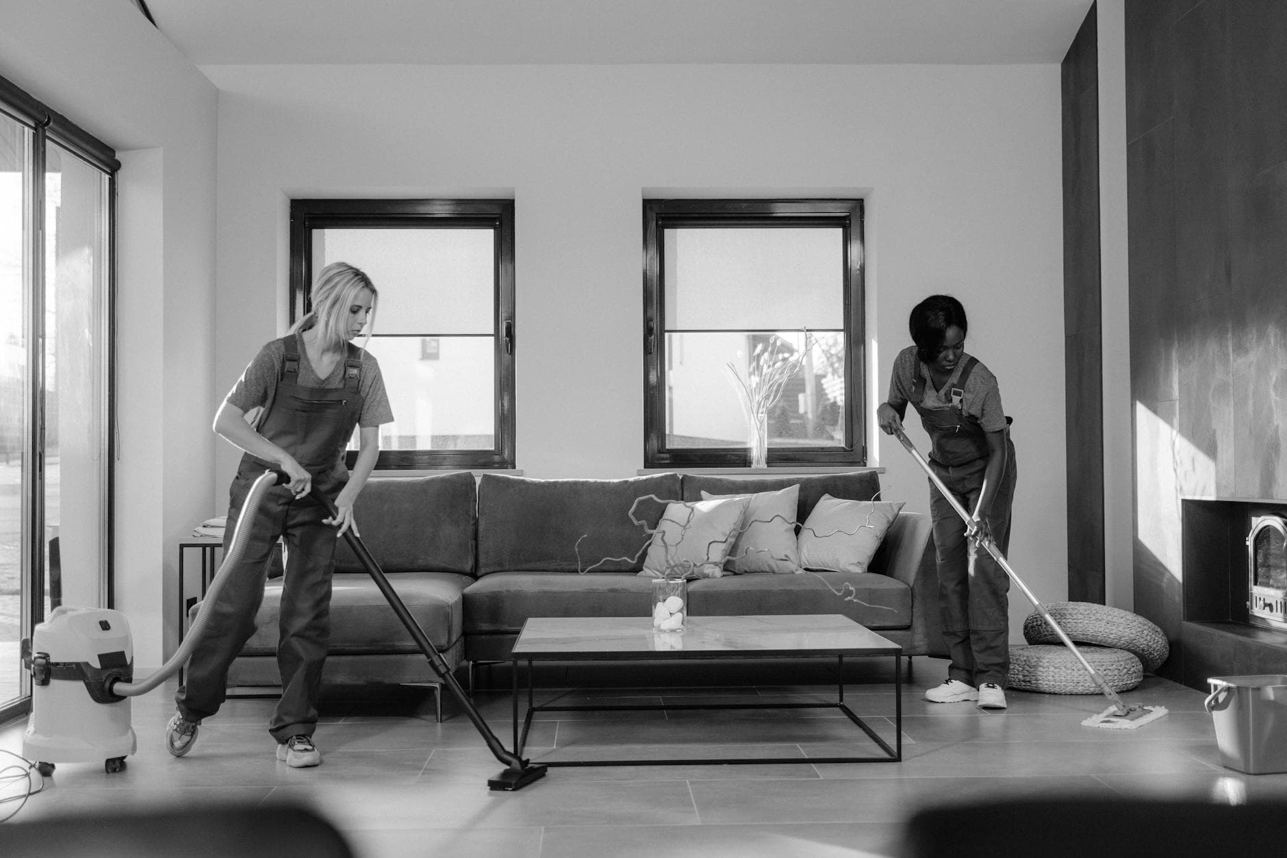 Two Your Business cleaners in work uniforms using a vacuum and mop in a modern Manhattan living room — Office Cleaning in Cliffside Park, New Jersey