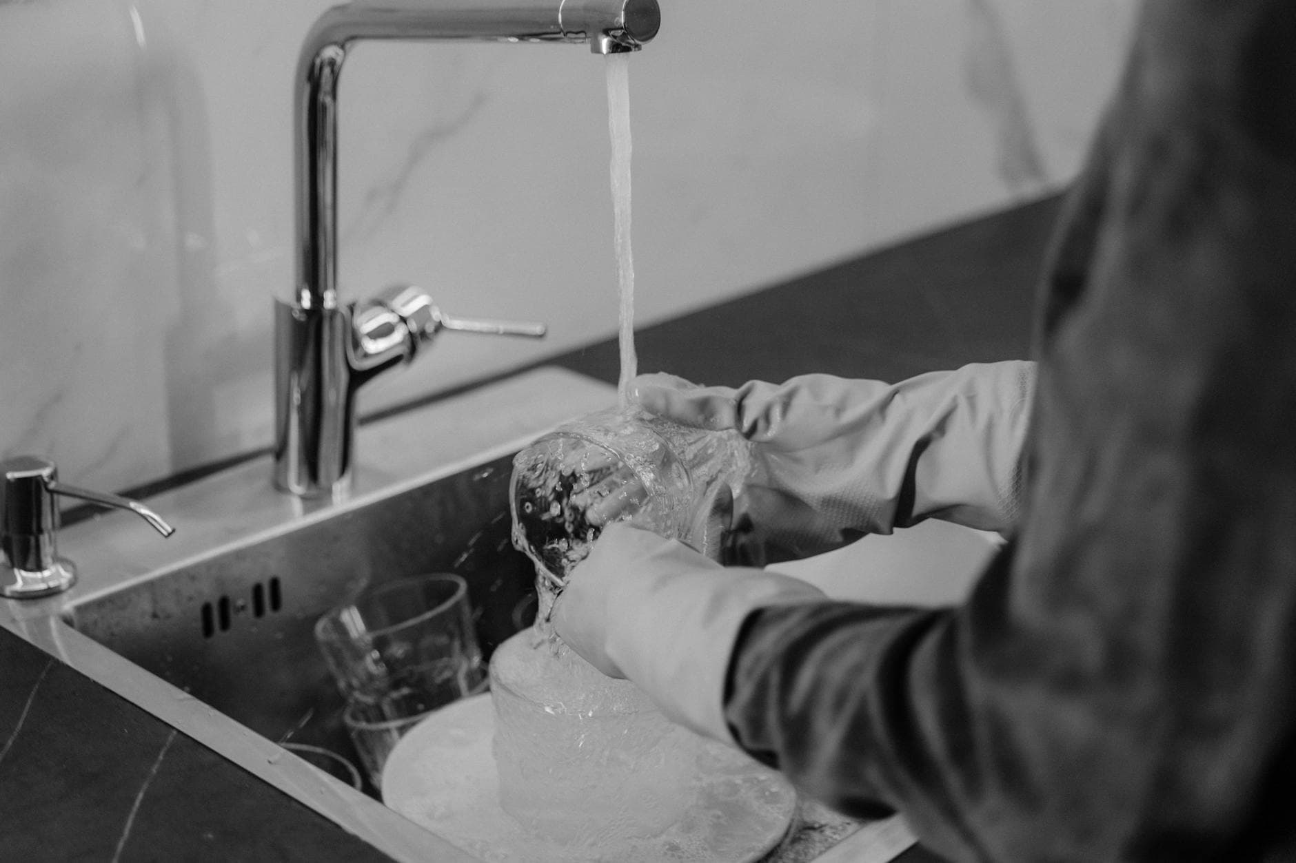 NYC kitchen cleaning service washing dishes under running water at the sink — cleaning services in Tarrytown, Westchester
