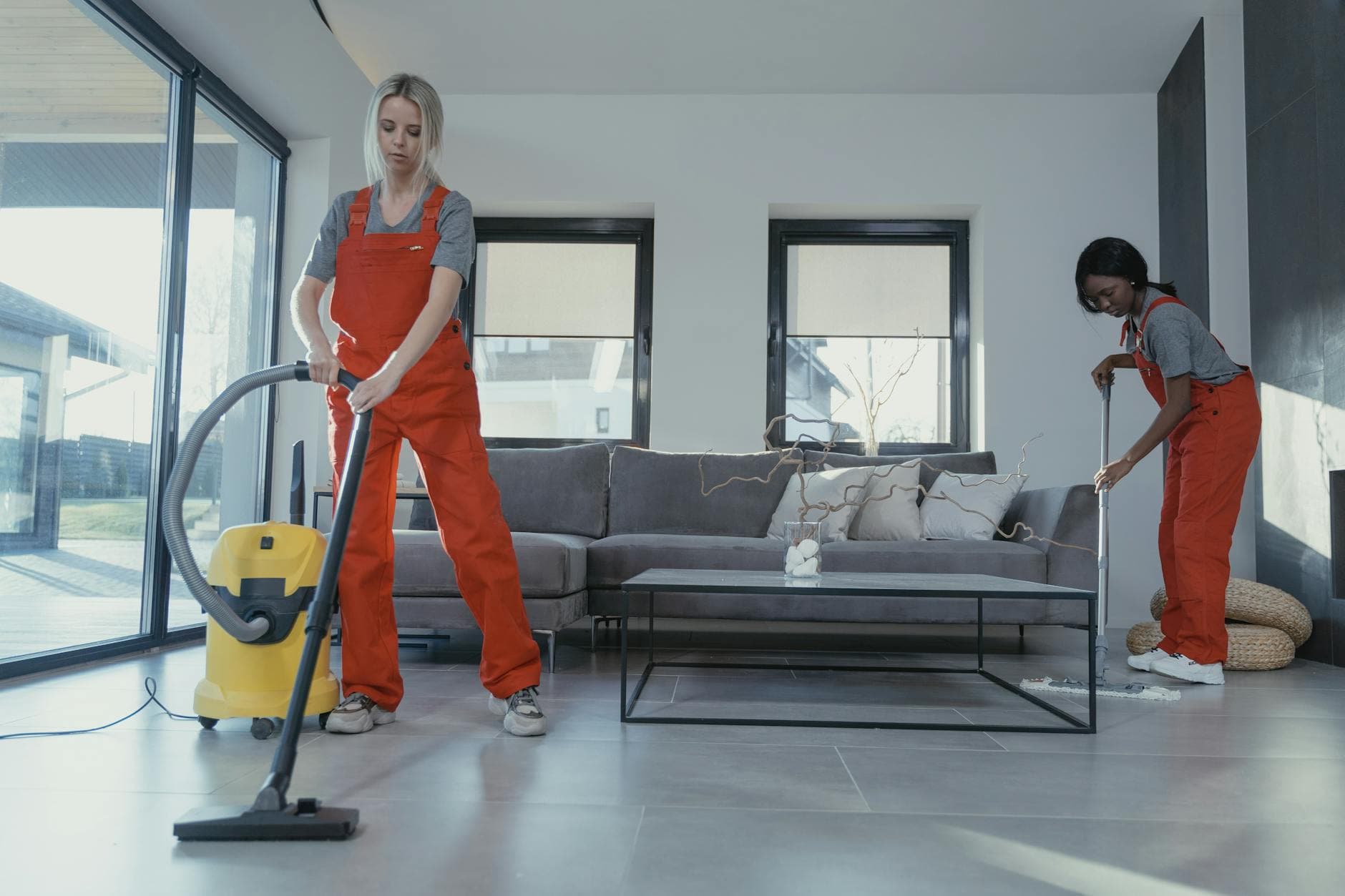 Two Your Business cleaners in red overalls vacuuming and sweeping a modern NYC living room — Move-In/Move-Out Cleaning in Cliffside Park, New Jersey