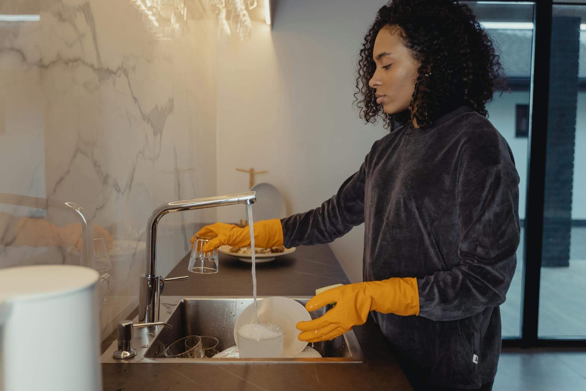 professional cleaner wearing rubber gloves washing dishes in a modern Manhattan kitchen — cleaning services in Ditmars Steinway, Queens